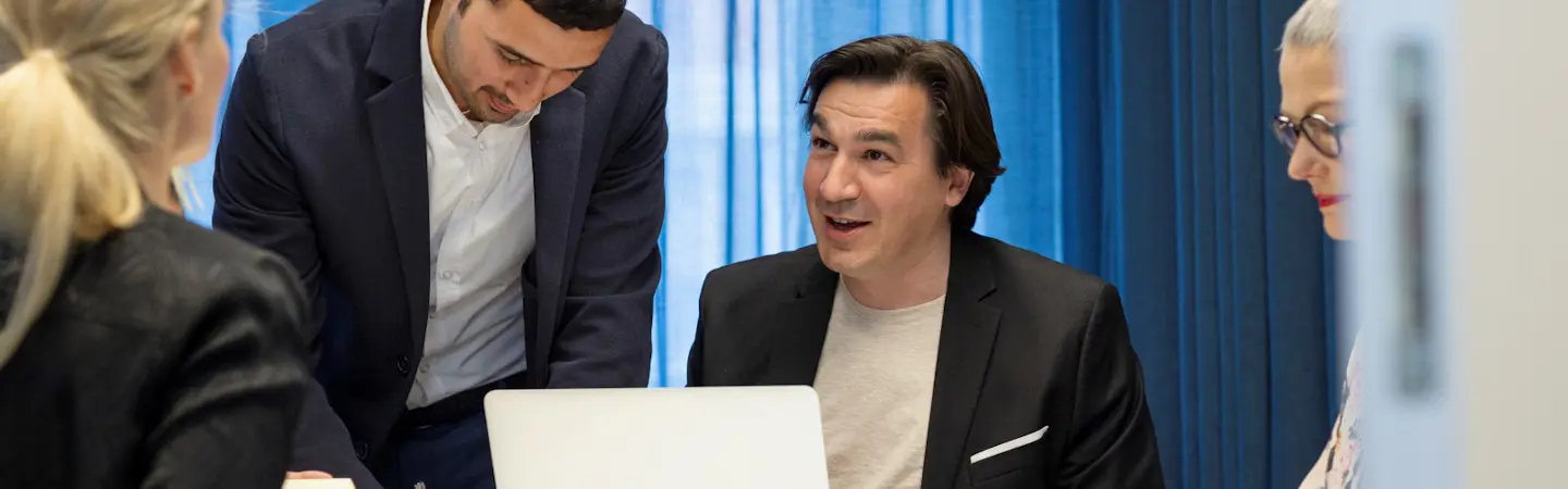 Fyra personer sitter vid ett bord vid en dator. De har kavajer på sig.