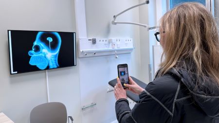 En kvinnlig person tar en bild av en skärm inne i ett vitt sjukhusrum.