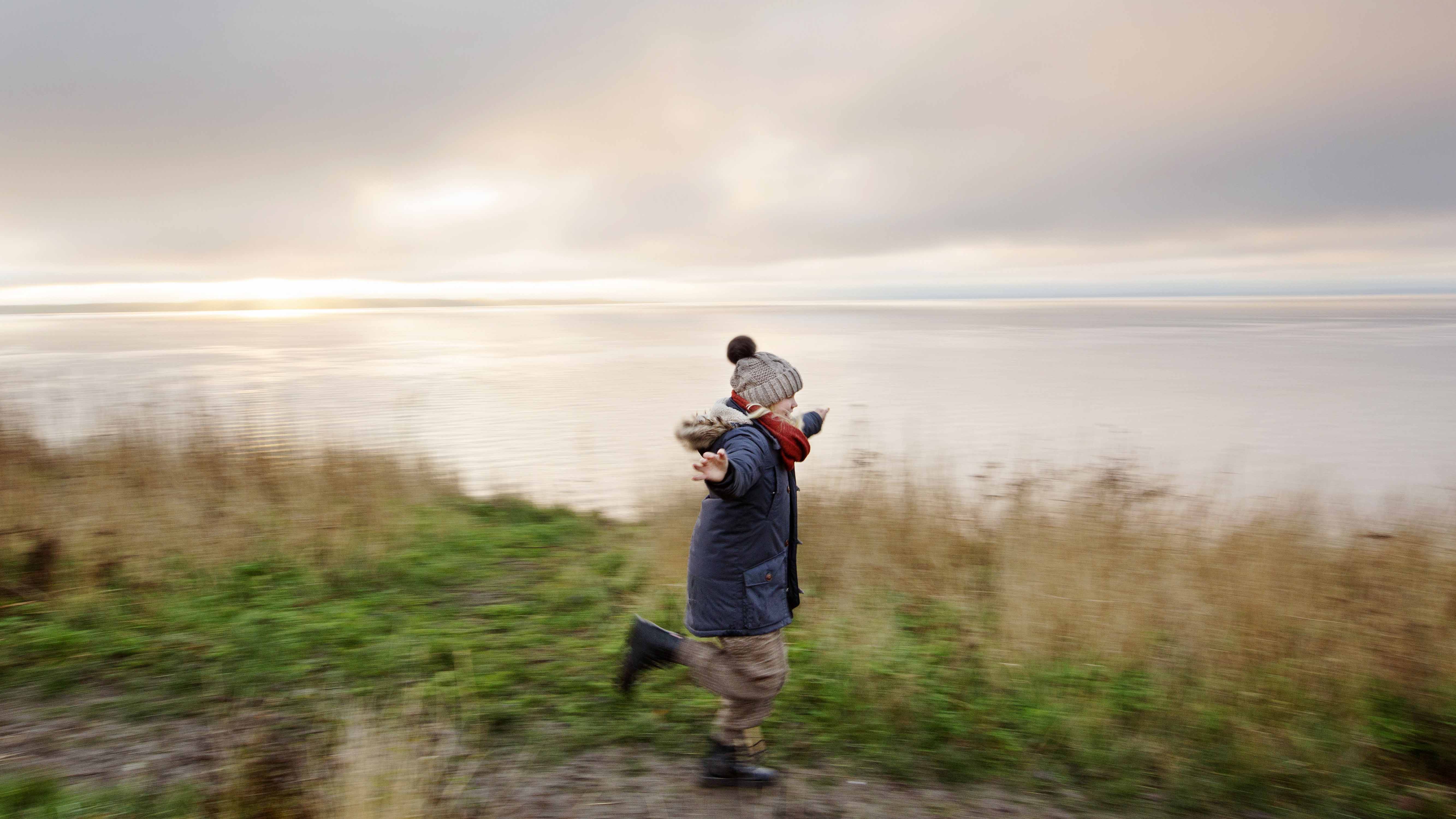 Flicka klädd i vinterkläder springer längs en strand.