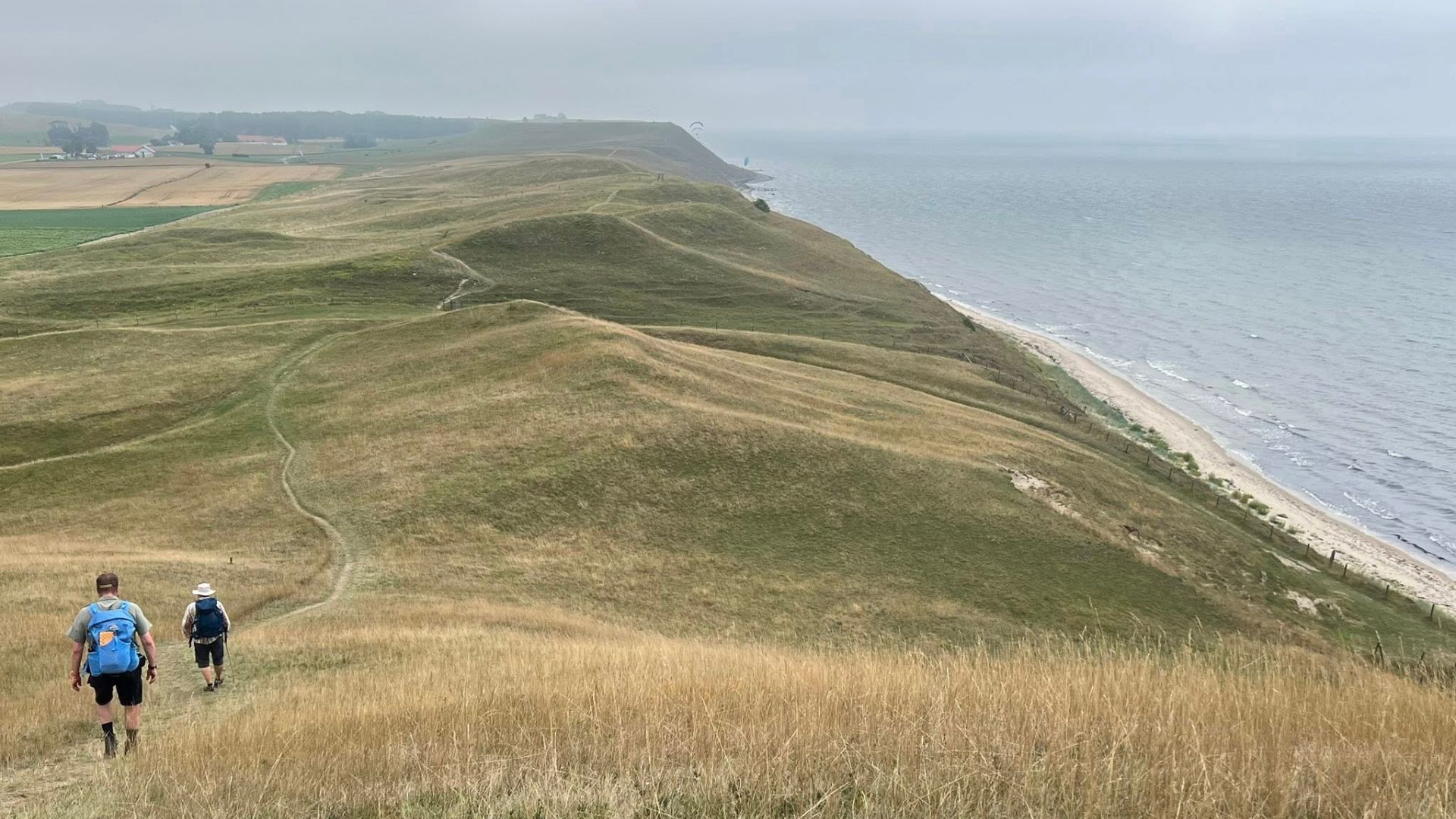 Två personer med ryggsäck vandrar längs en led vid vattnet. 