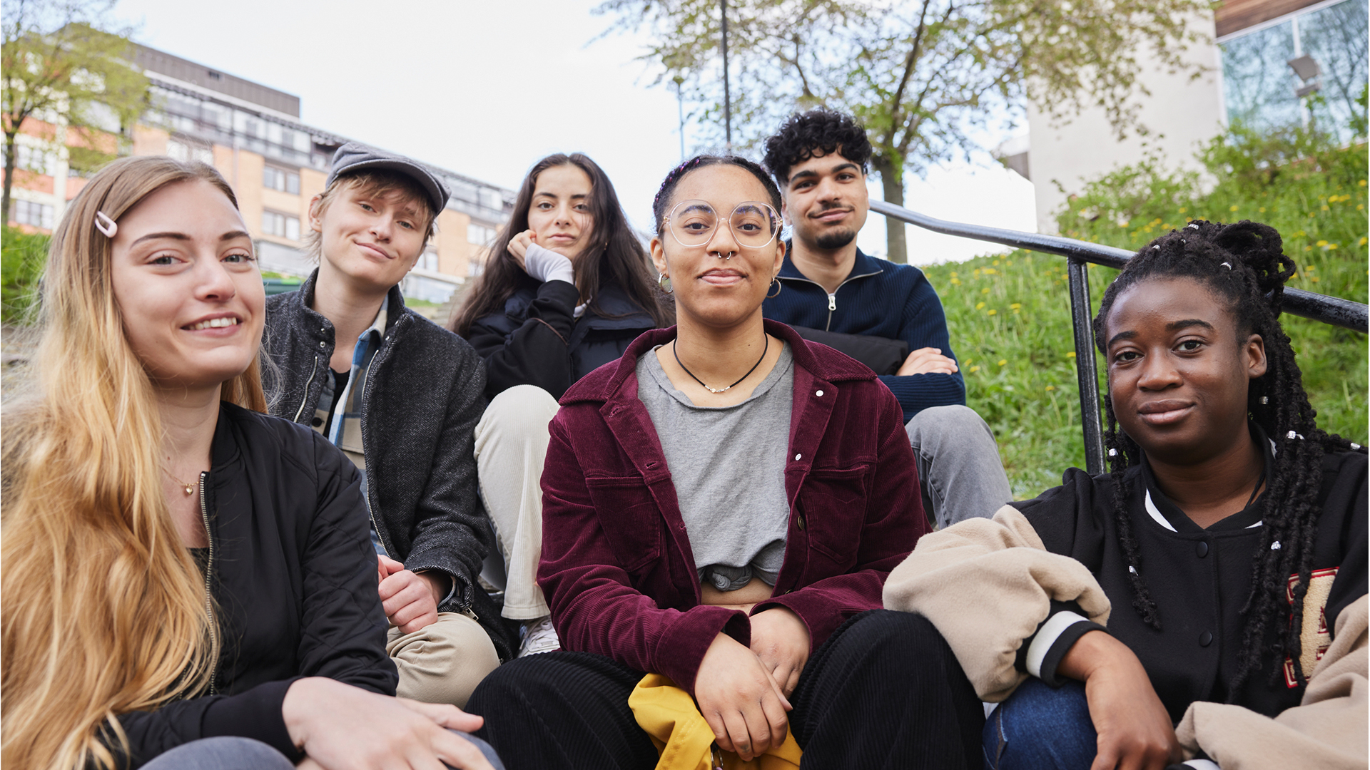Sex tjejer och killar som sitter utomhus i en trappa