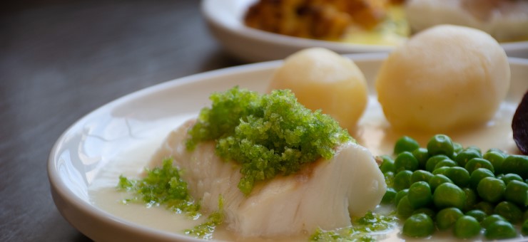 Närbild på kokt potatis, ärtor och en bit fisk upplagda på en tallrik.