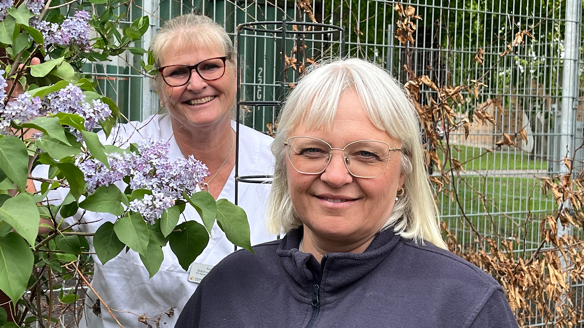 porträttbild på Anette Lindberg och Annika Lindblom, som är rehabundersköterskor  stående vid en syrenbuske