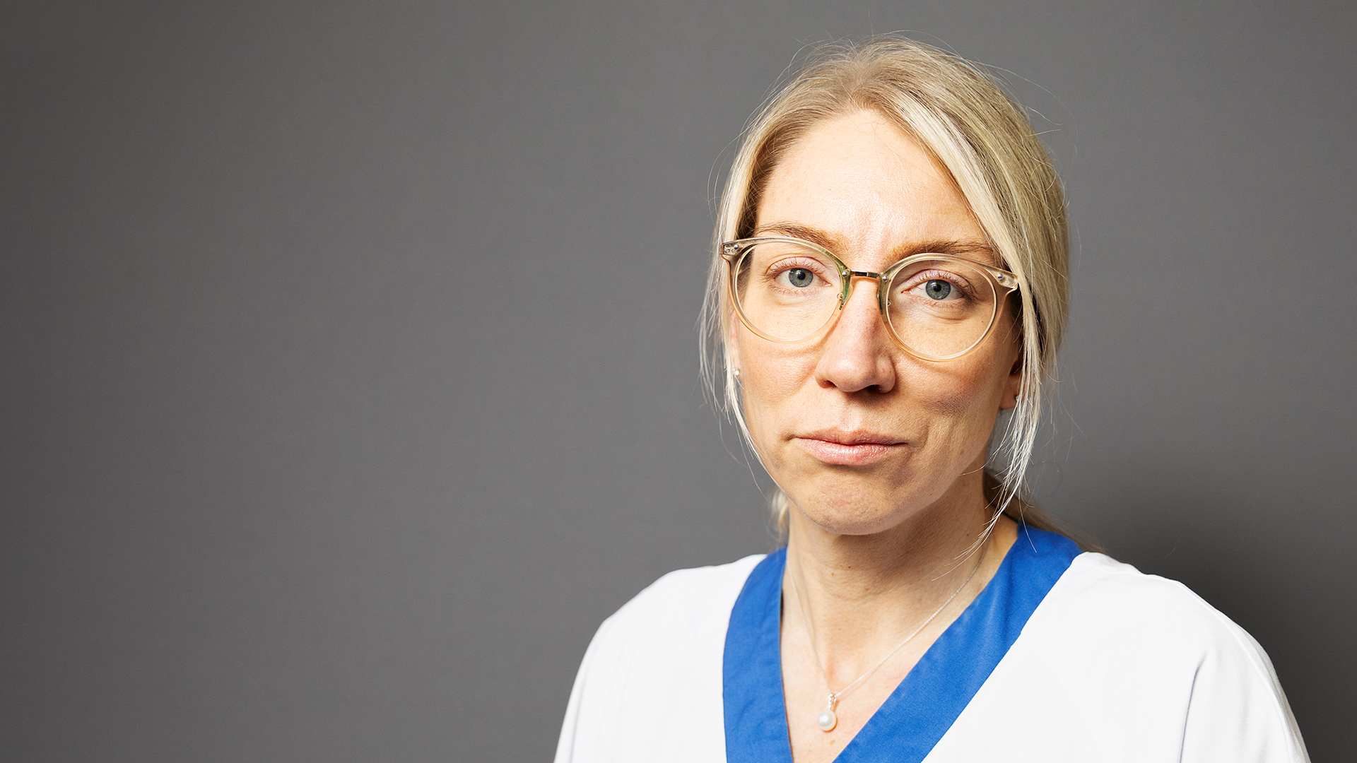 Person i läkarrock tittar in i kameran. 