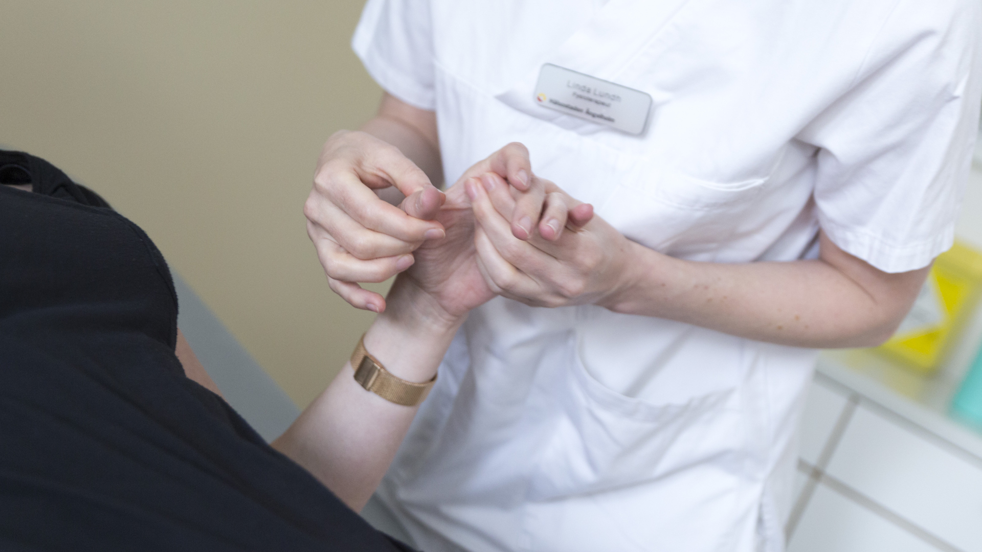 Närbild på sjukgymnast i vårdkläder som undersöker händerna på patient