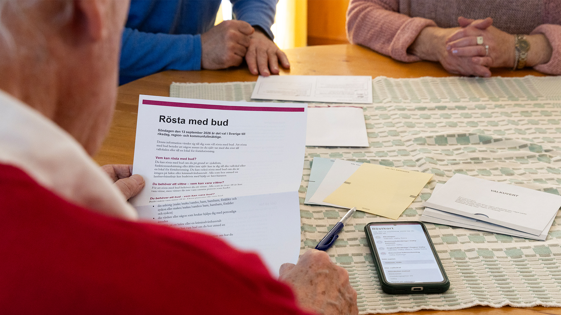 Person sitter vid bord och håller i material med information om budröstning.