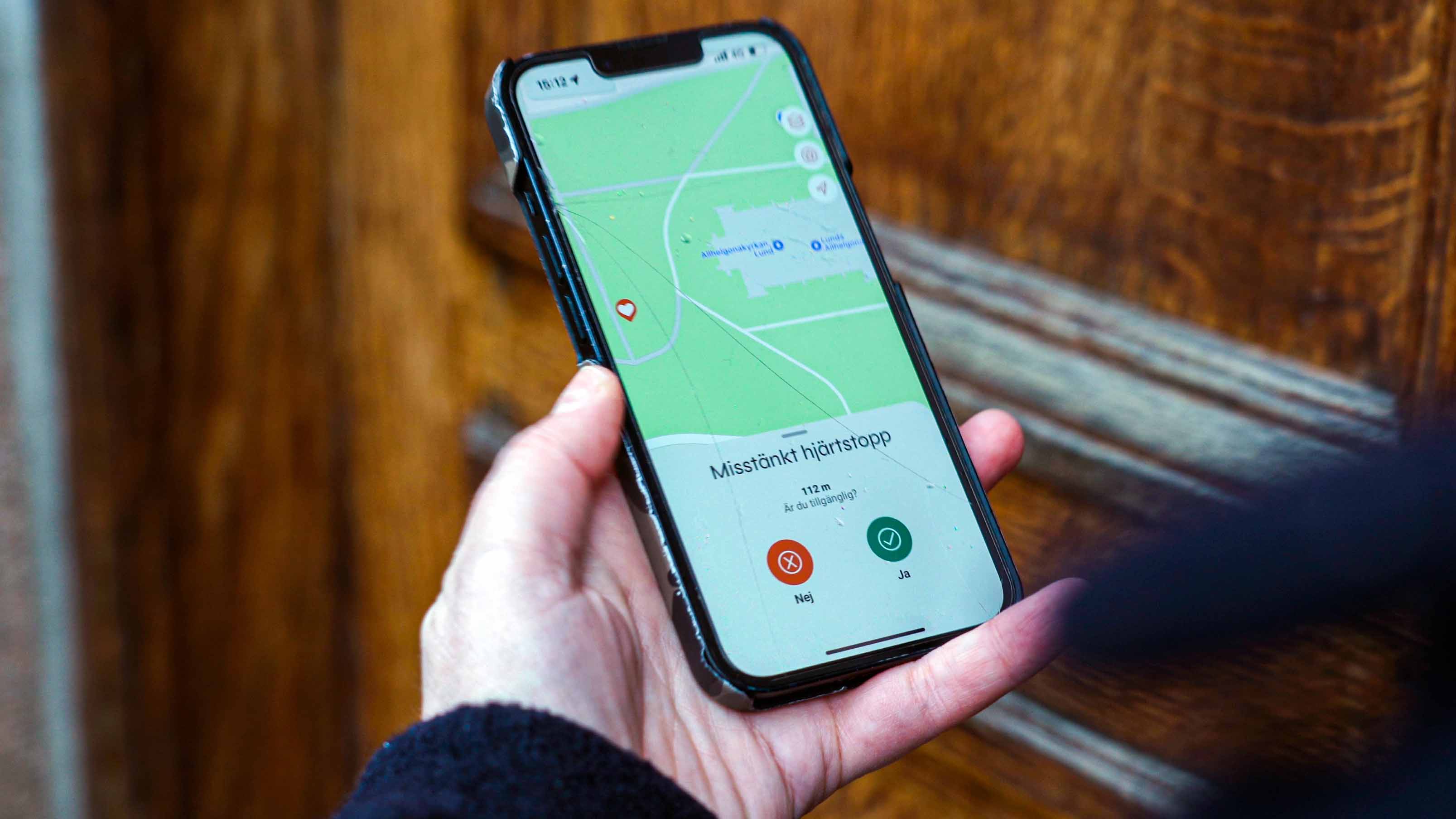 En hand håller i en mobil där det informeras om ett misstänkt hjärtstopp