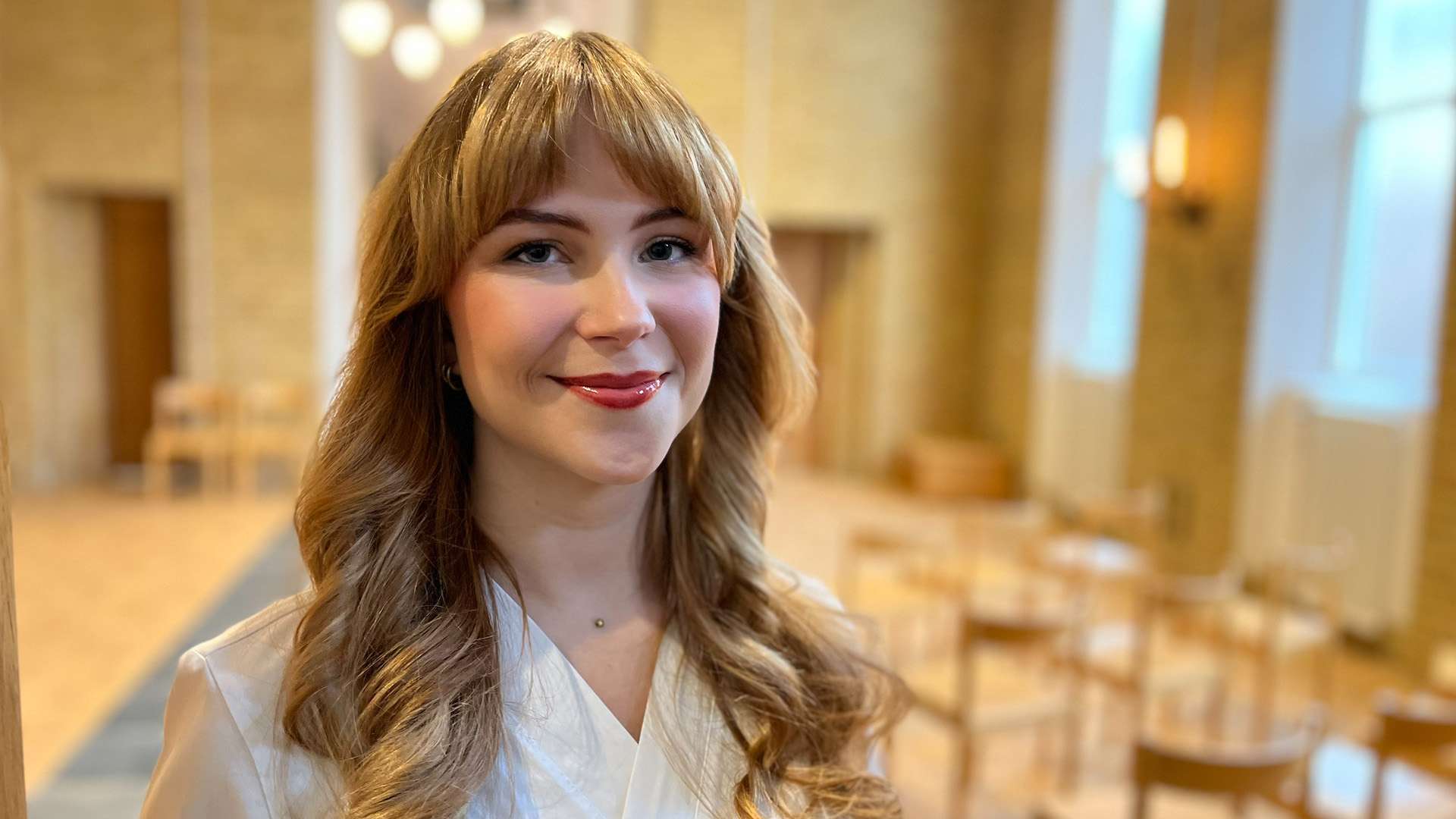 En person står i ett rum och tittar in i kameran.