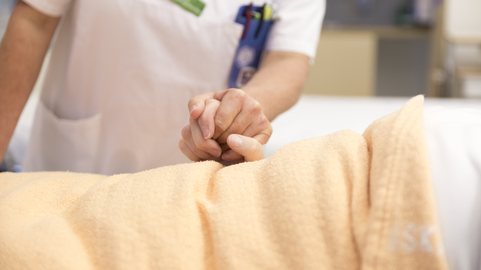 Närbild på vårdpersonal i vita kläder som håller i en patients hand