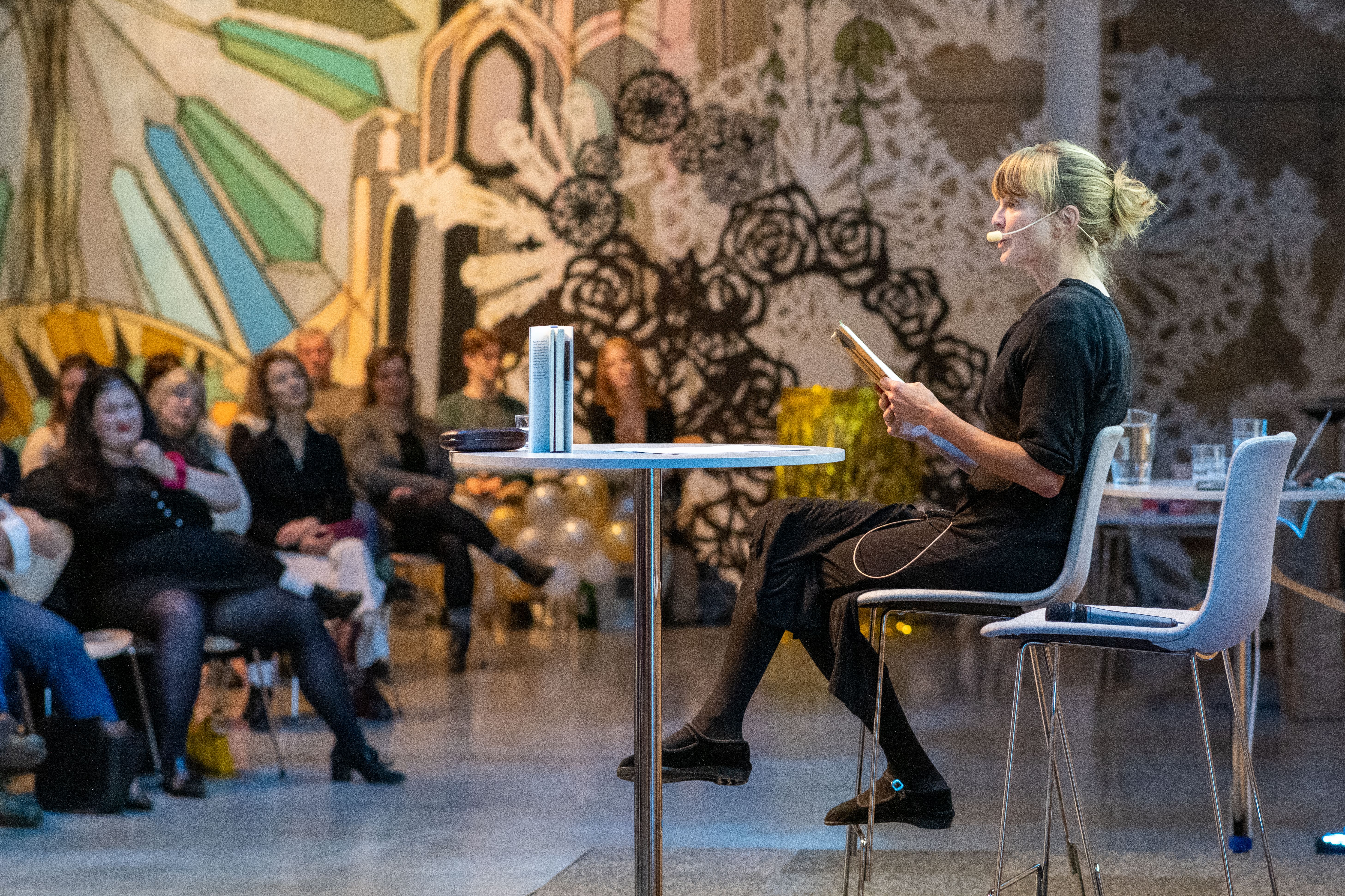 En person sitter på en scen och föreläser för en publik.