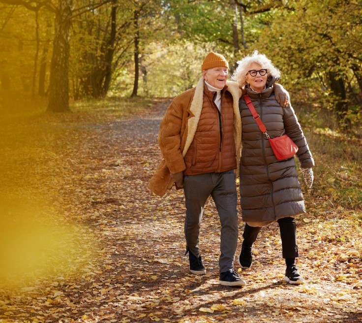 två äldre personer går tätt tillsammans i en höstfärgad skog.
