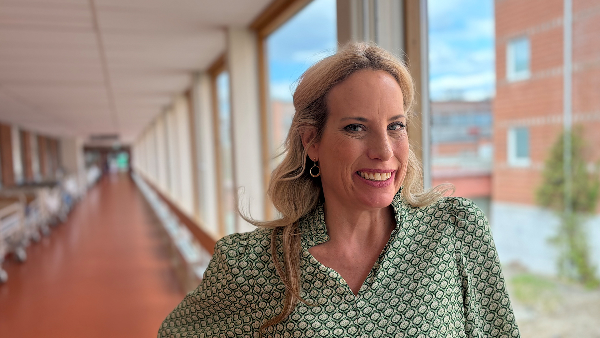 Porträttbild på leende Andrea Borgström som står i en sjukhuskorridor.