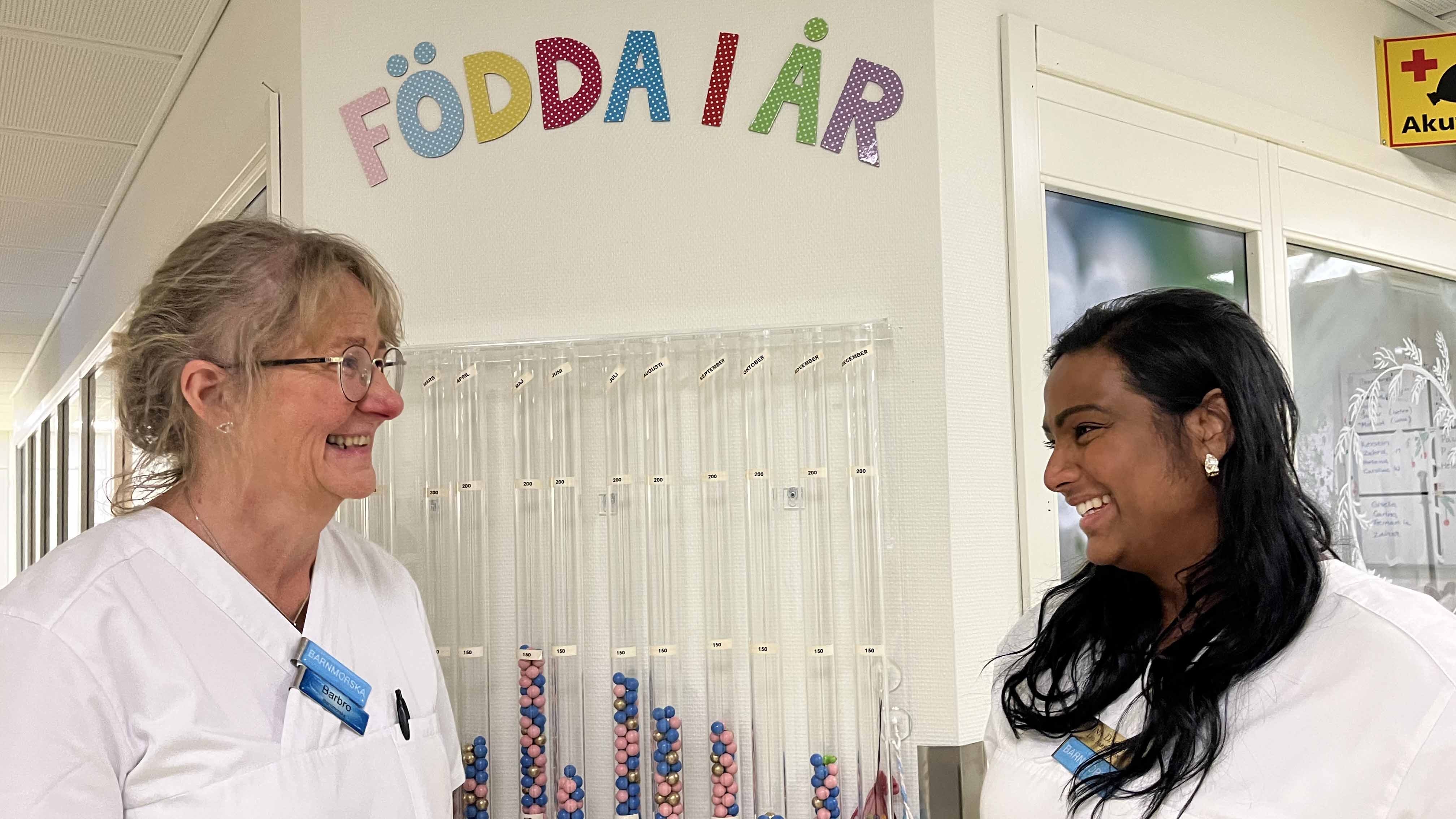 barnmorskor på förlossningsavdelning fram för en skylt där det står "födda i år" och kulor som representerar de födda