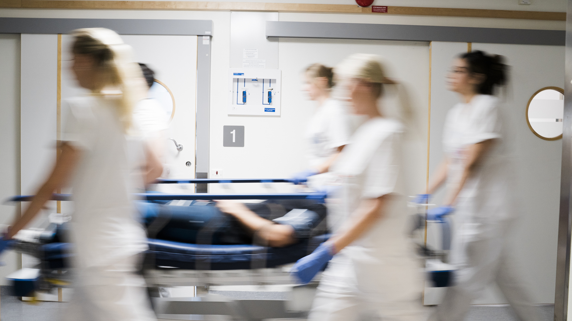 Vårdpersonal kör en patientsäng i en korridor