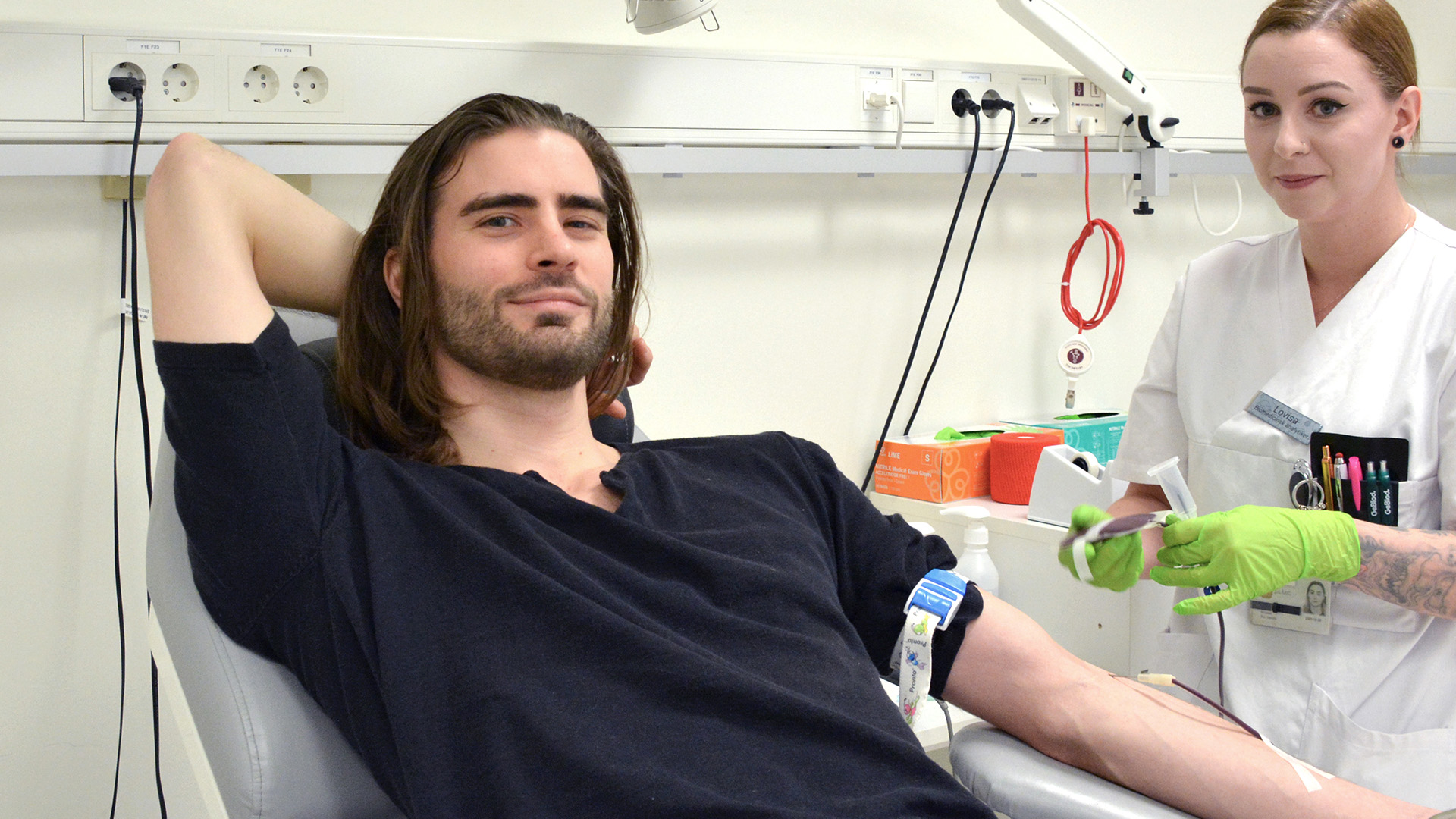 En man ligger på en brits och ger blod. En sköterska står bredvid.