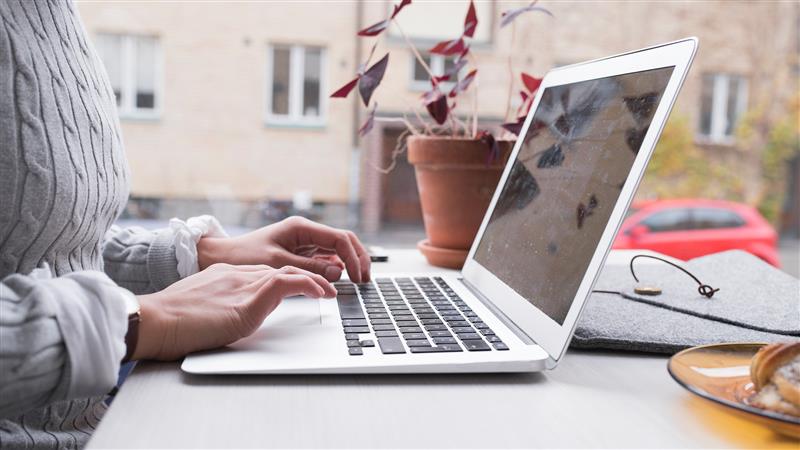 En person sitter vid ett bord och skriver på en laptop.