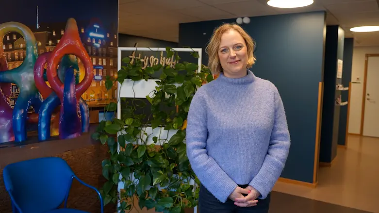 En kvinna står framför en växt och tittar in i kameran