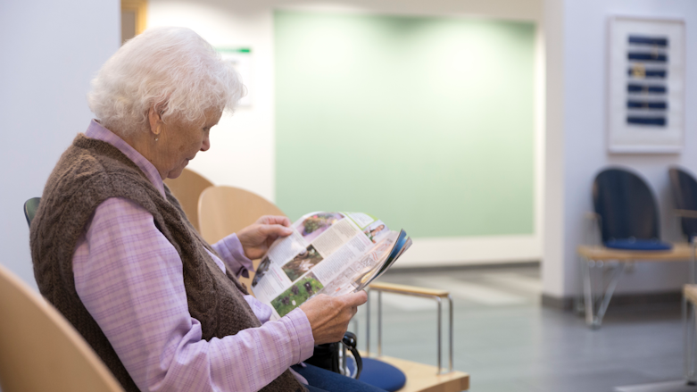 En person sitter i ett väntrum och läser en tidning.