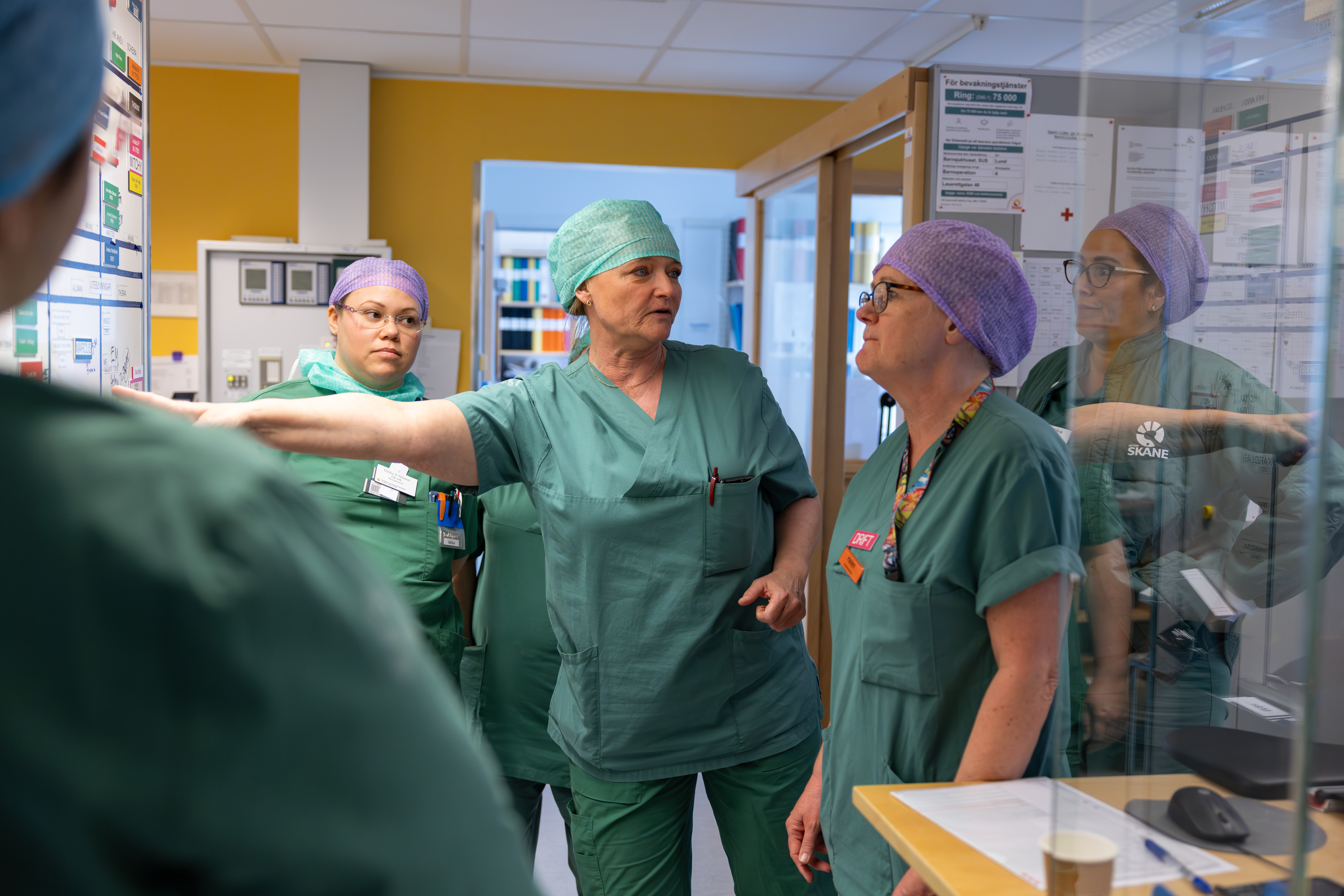 Vårdpersonal står framför en planeringstavla iklädda operationskläder i sjukhusmiljö.