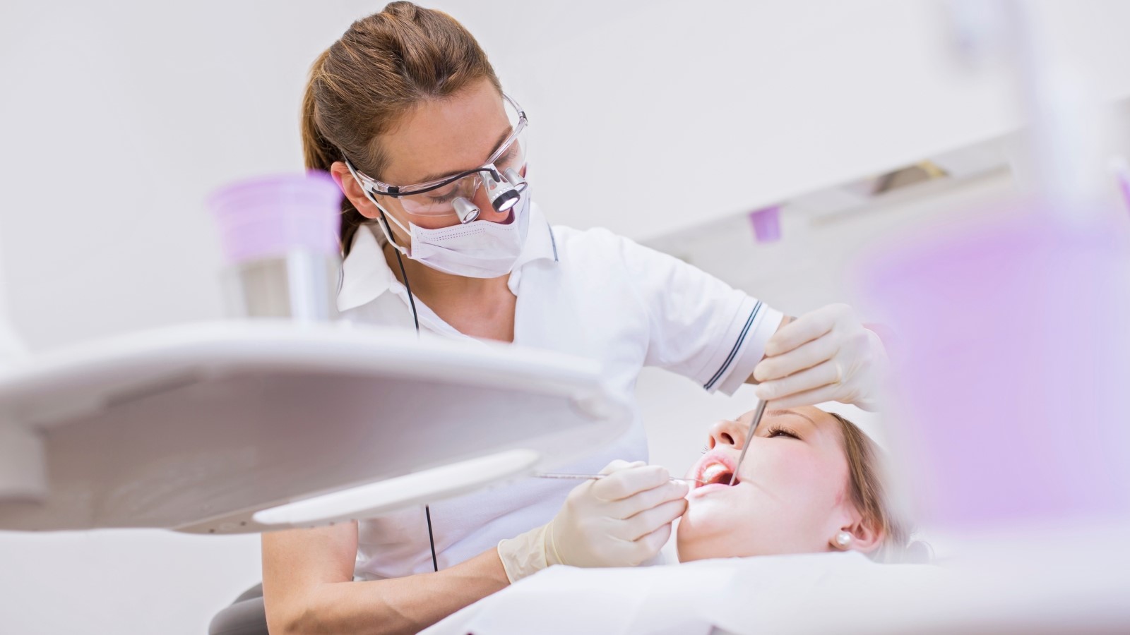 En tandläkare står böjd över en patient och undersöker patientens tänder.