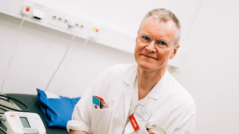 En manlig person i läkarkläder tittar in kameran