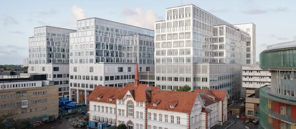 stadsmiljö med tre husbyggnader med ljus fasad som reser sig ovanför lägre byggnader