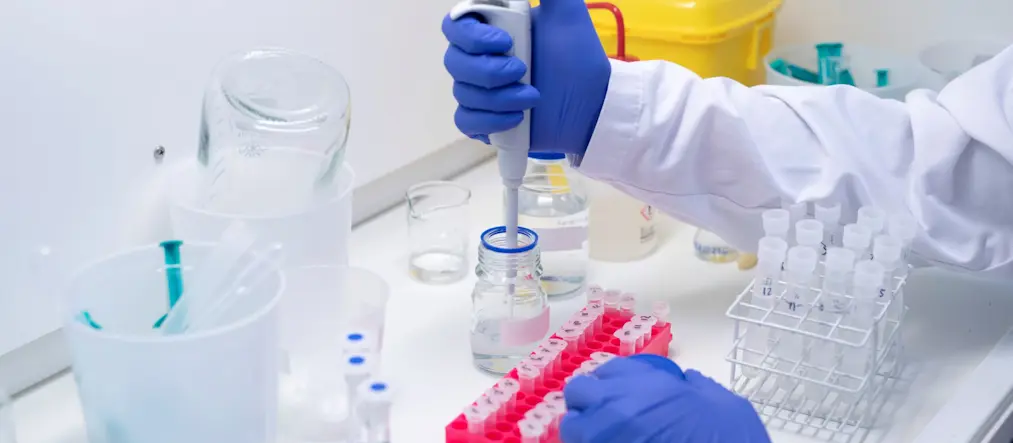 Forskare med gummihandskar fyller på ett prov.