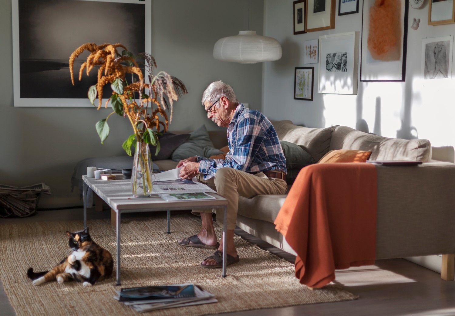 En äldre man sitter i ett vardagsrum och läser.