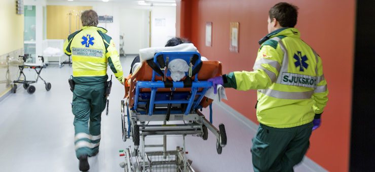 Två ambulanssjukvårdaren rullar in bår i sjukhuskorridor