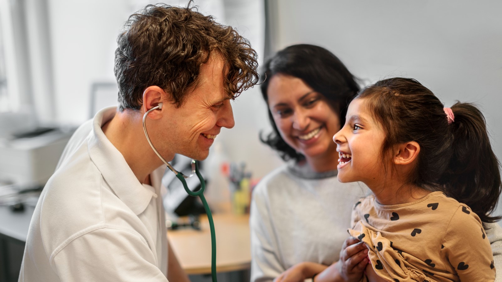Läkare undersöker en skrattande flicka med ett stetoskop. 