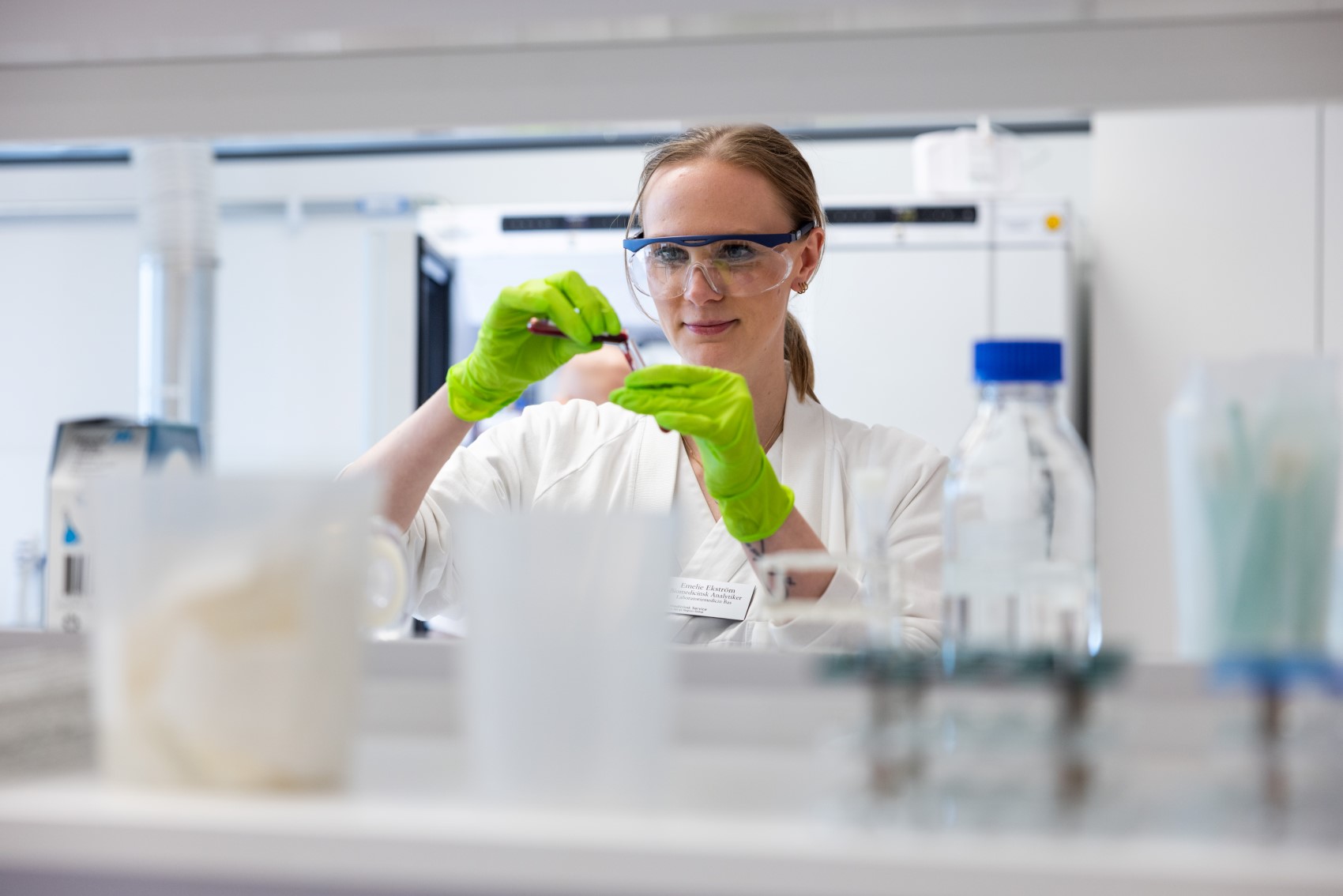 Kvinna med skyddsglasögon och handskar i laboratoriemiljö.