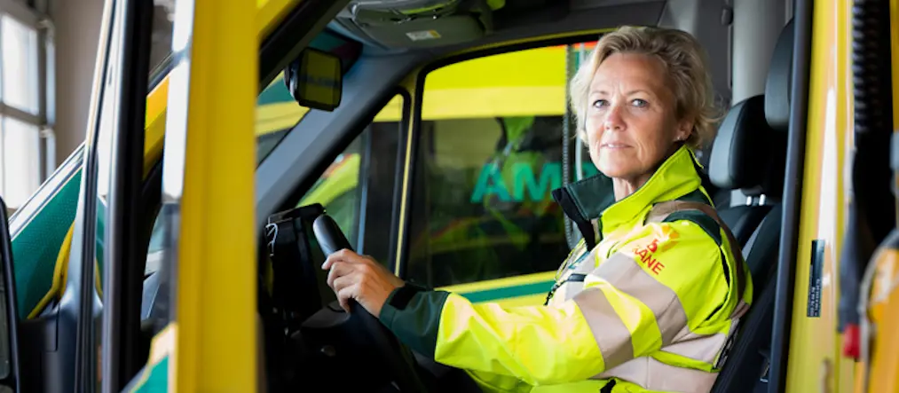 En kvinna sitter i arbetskläder vid ratten på en ambulans