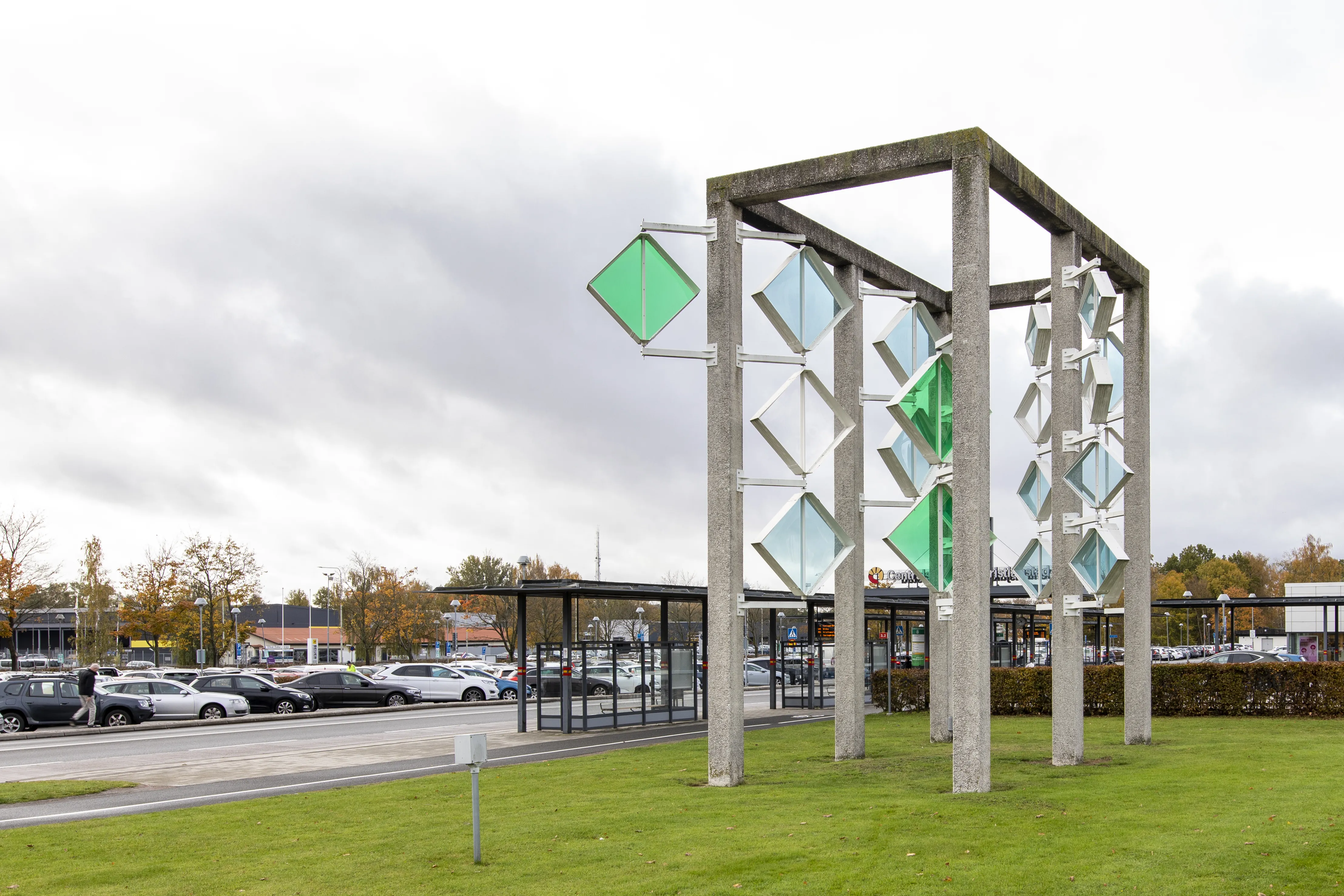 På en gräskulle står en skulptur i form av en betongram med färgade plexiglasskivor som dekoration.