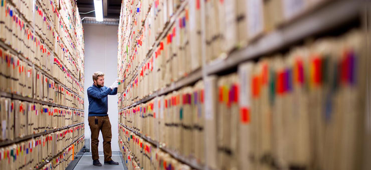 Man står i arkivrum med hyllor fyllda med mappar. Foto: Christiaan Dirksen
