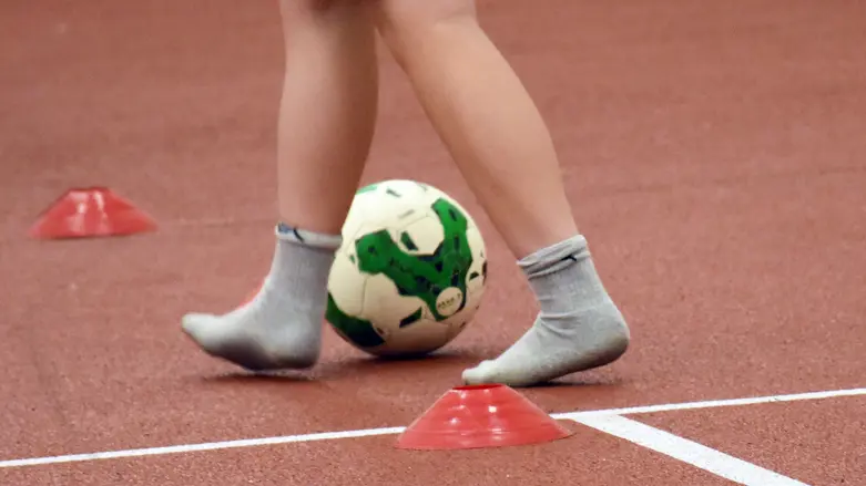 ett barn dribblar en fotboll mellan två orangea koner. Fotot är från knäna och nedåt.
