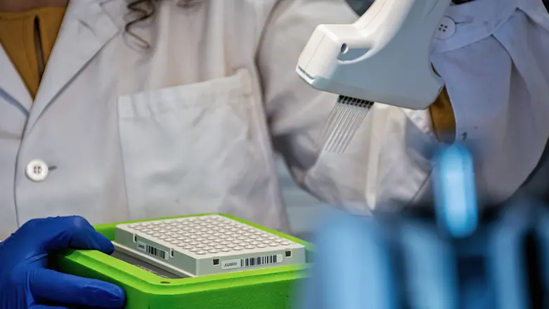 närbild på handskbeklädda änder som håller i laboratorieutrustning