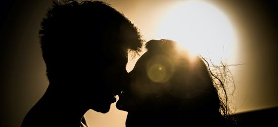 Två personer som kysser varandra fotade i profil i motljus
