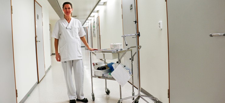 Kvinna i vit sjukvårdsrock kommer gående i sjukhuskorridor.