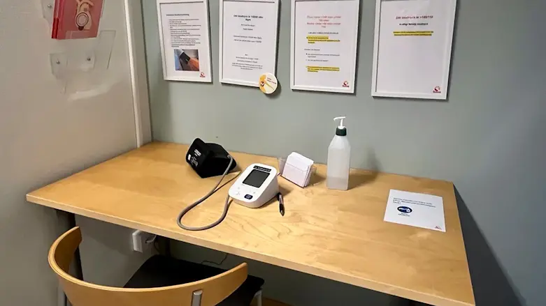 Foto från en vårdcentral där man ställt i ordning en hörna för att mäta sitt blodtryck, med bord, stol, blodtrycksmätare och handsprit.