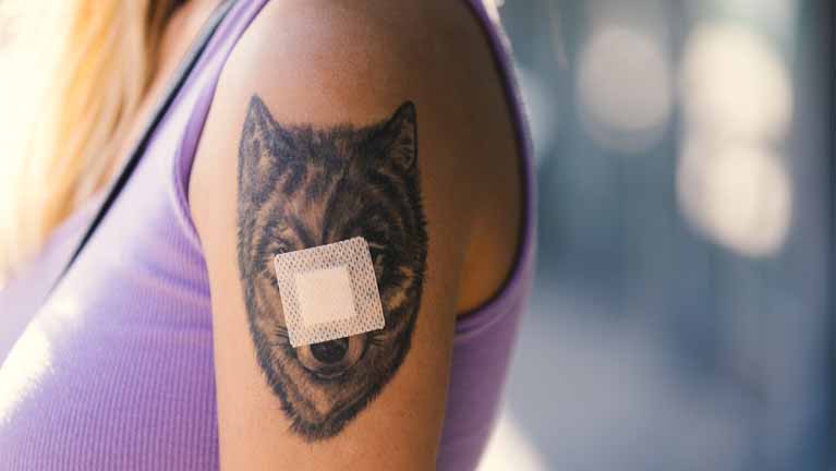 en kvinnas överarm med en tigertatuering och ett plåster från spruta mitt över tatueringen.