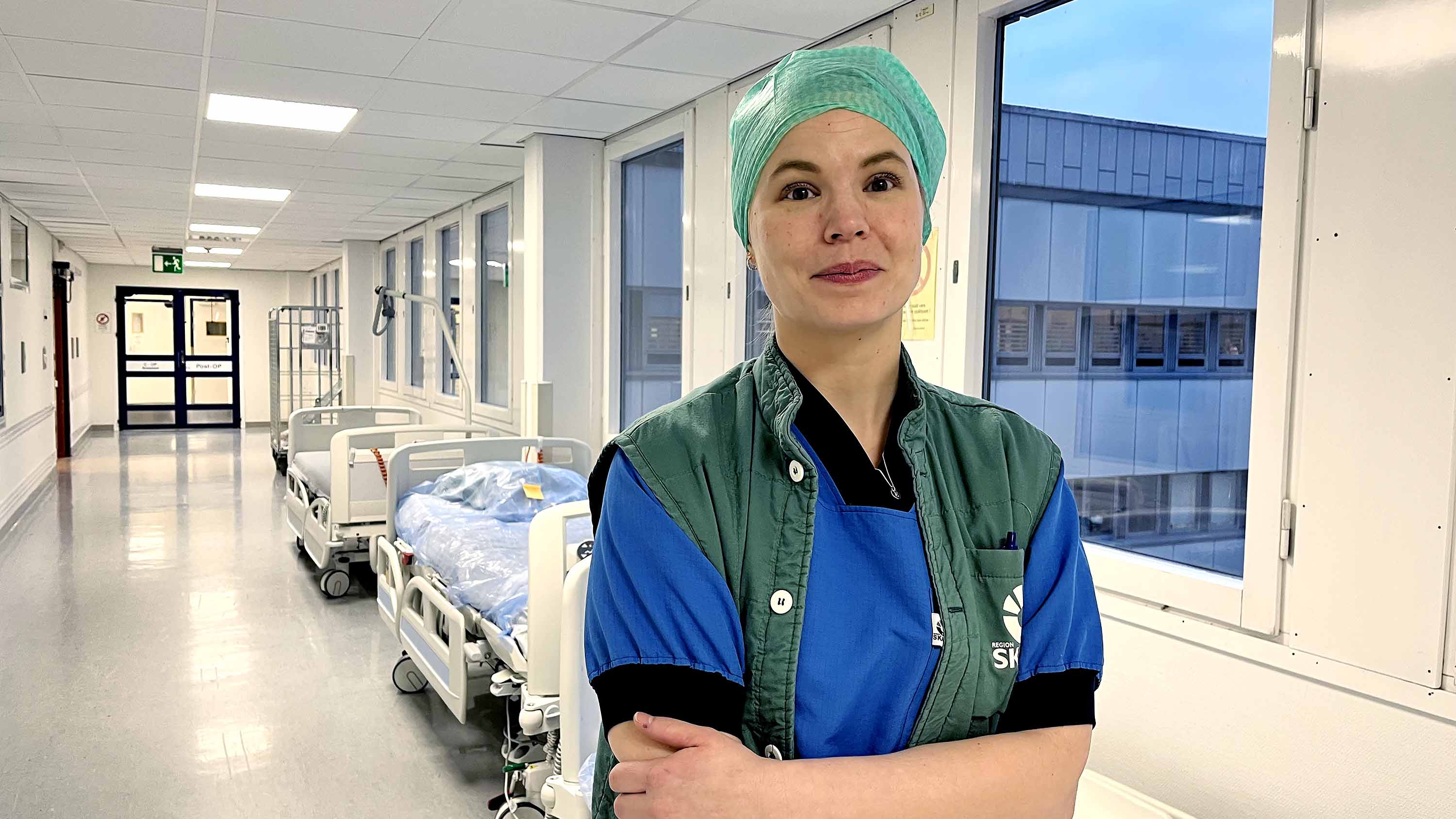 Läkaren Karin Falbrink står i en sjukhuskorridor klädd i gröna och vita vårdkläder.