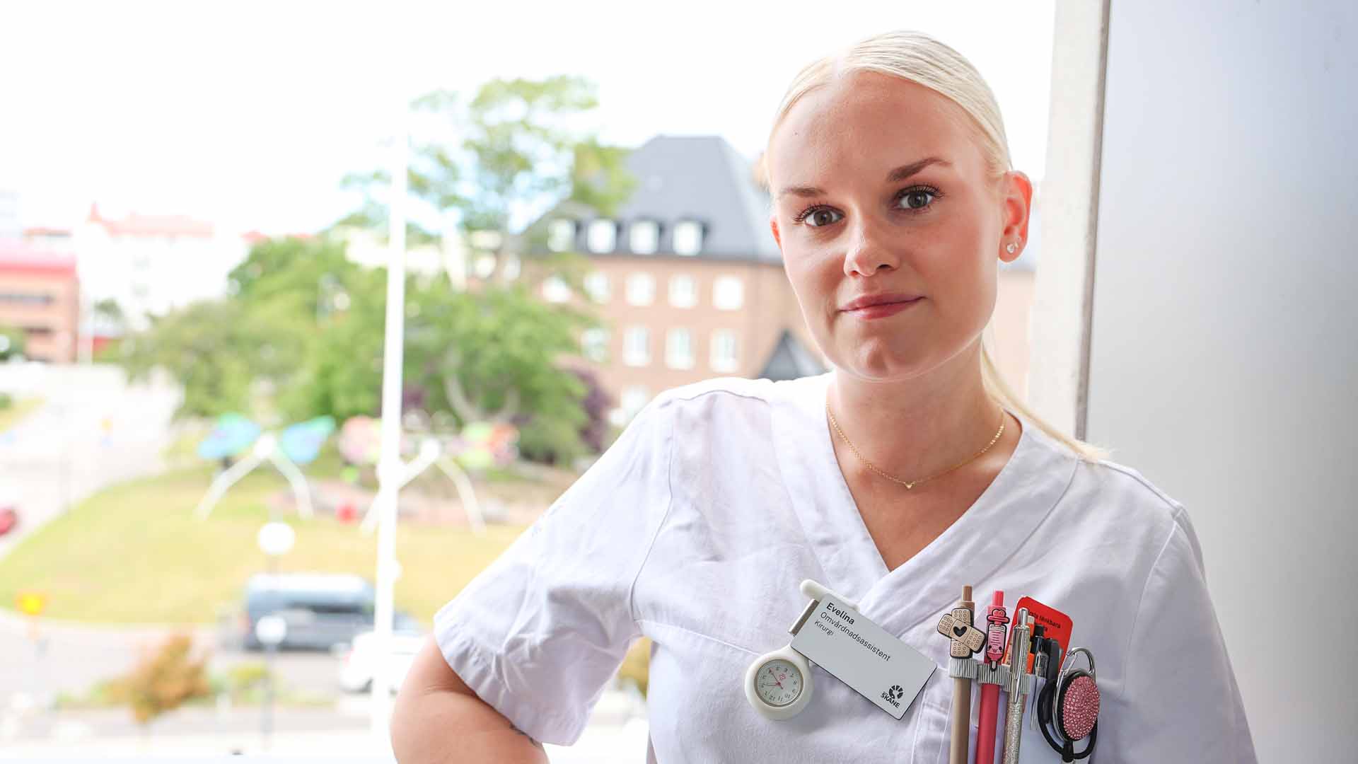 Evelina Nilsson klädd i vita vårdkläder, står framför ett fönster.