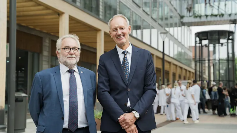 Regiondirektör Lars-Åke Rudin och fastighetsdirektör Pål Svensson klädda i kostym framför fasaden till nya vårdbyggnaden i Malmö.