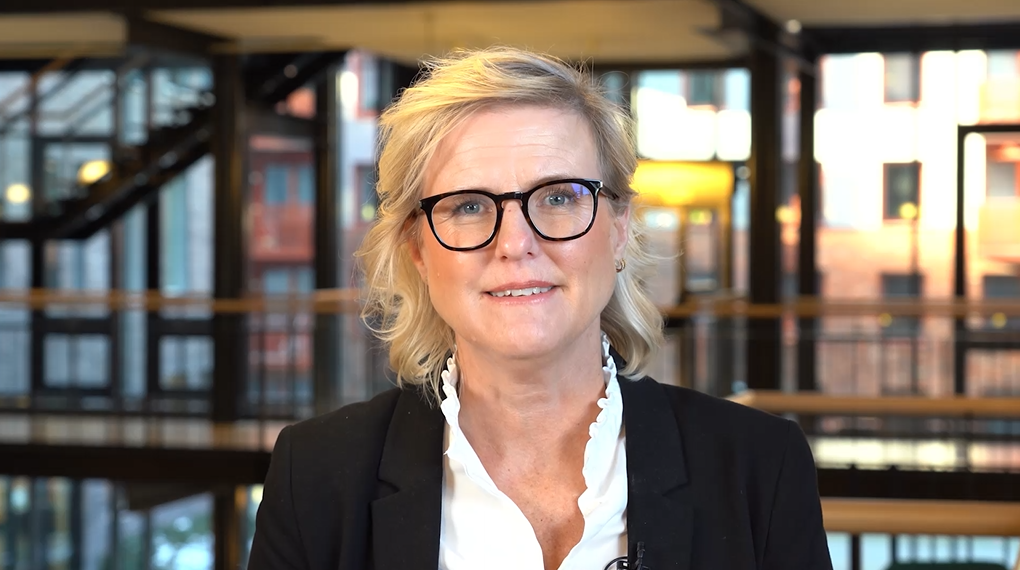 Karin Cedwall, klädd i vit blus och svart kavaj, tittar in i kameran.