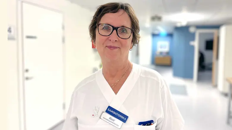 Sjuksköterskan Kerstin Reistad klädd i vita vårdkläder i sjukhuskorridor.
