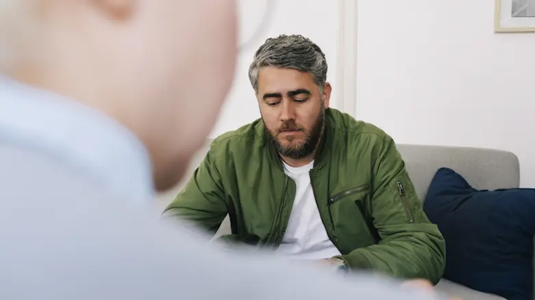 man i grön skjorta sitter i ett behandlingsrum och ser deprimerad ut. I förgrunden en kvinna som troligen är vårdpersonal.