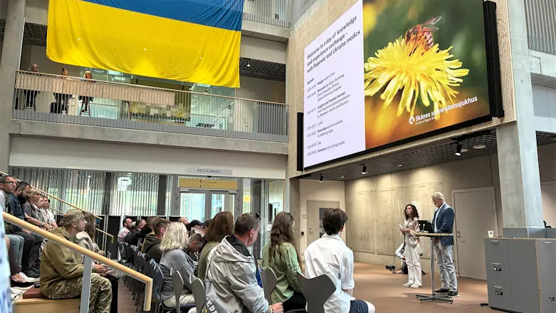 Ukrainska och svenska sjukvårdare sitter tillsammans i en föreläsningssal på Skånes universitetssjukhus i Malmö. En stor ukrainsk flagga pryder långsidan av rummet.