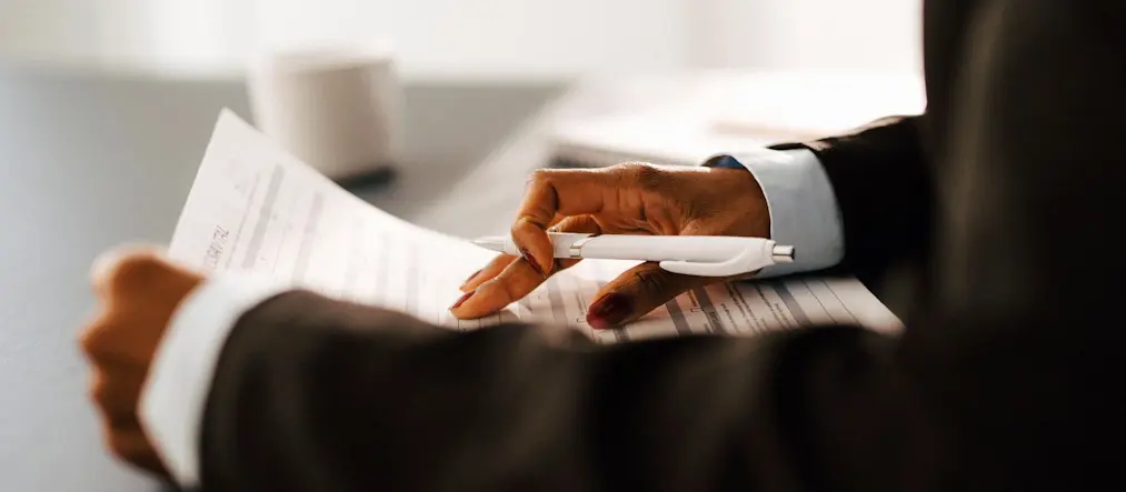 En person läser papper, hen håller en penna i ena handen, man ser bara de kavajklädda armarna.