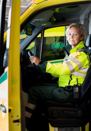 En kvinna sitter i arbetskläder vid ratten på en ambulans