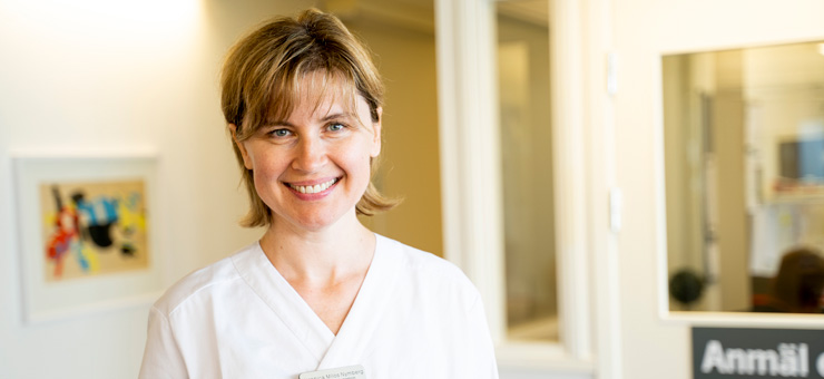 En leende kvinna i arbetskläder står i vårdmiljö